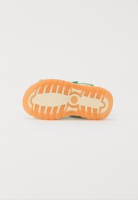 Green sneaker sole with a textured pattern, featuring an orange outsole and white midsole. The tread has distinct grooves for traction.