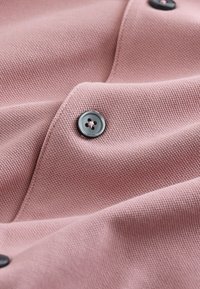 Tessuto rosa tenue con trama testurizzata, caratterizzato da bottoni scuri con design a quattro fori, che mettono in risalto i dettagli della cucitura.