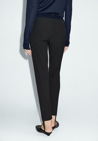 Pantaloni neri su misura con vestibilità slim e texture liscia. Presentano cuciture minime e due tasche posteriori. Abbinati a scarpe nere senza lacci.
