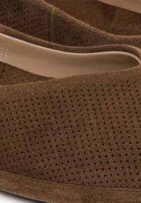 Hnědé semišové slip-on boty s texturovaným, perforovaným designem a hladkým vnitřním podšitím. Zaoblený tvar, nízkoprofilové podrážky.