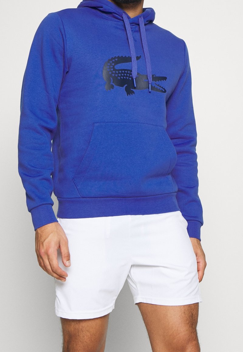 Felpa blu realizzata in misto cotone, caratterizzata da una tasca a marsupio, cappuccio con cordino e una grafica di coccodrillo nera sul fronte.