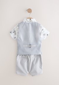 Chaleco gris claro con una camisa de manga corta de flores, combinado con pantalones cortos gris a cuadros. Cuenta con una hebilla en la espalda y tela con textura.