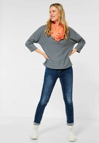 Top a maniche tre quarti con patttern houndstooth in bianco e nero, abbinato a jeans di denim scuro e a una sciarpa infinita arancione. Sneakers bianche.