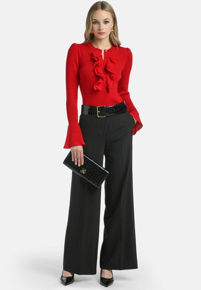 Pulover roșu cu dungi, cu detalii volan, asortat cu pantaloni negri cu picioare largi și tocuri negre lustruite. Accesoriile includ o geantă de mână neagră.