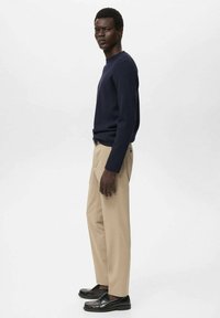 Jersey azul marino, pantalones beige y mocasines negros. El jersey es ajustado, de manga larga; los pantalones tienen un corte recto y una textura suave.