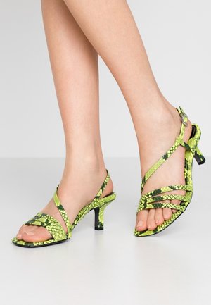 Zielone sandały na wysokim obcasie w wężowy wzór, z krzyżującymi się paskami, otwartym noskiem i smukłym obcasem. Teksturowany materiał z błyszczącym wykończeniem.
