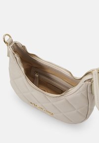 Quiltad beige handväska i syntetmaterial med gulddragkedja och -detaljer. Inuti finns en ficka utan dragkedja och ett fack med dragkedja.