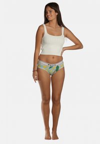 Haut court blanc en tricot avec encolure carrée, associé à un sous-vêtement bleu avec un motif de bananes jaunes et une ceinture "WAXX".