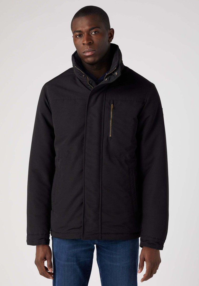 Czarna kurtka z wysokim kołnierzem, poziomymi szwami, zamkniętą kieszenią na piersi i gładką teksturą, w połączeniu z niebieskimi dżinsami.