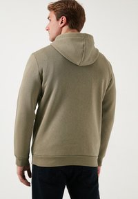 Olivovo zelená mikina s kapucňou vyrobená z mäkkej látky, so sťahovacou kapucňou, rebrovanými manžetami a voľným strihom. Hladká textúra; minimalistický dizajn.