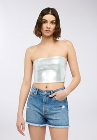 Crop top senza spalline di colore argento metallico abbinato a pantaloni corti in denim blu strappati. Il top presenta una texture liscia e lucida e un design aderente.