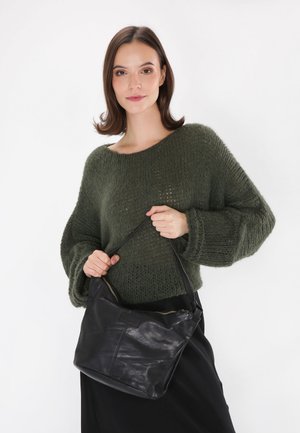 Zwarte leren handtas met een zachte textuur en een rits bovenaan, casual vastgehouden. Draagt een losse, gebreide olijfgroene trui. Eenvoudig, praktisch ontwerp.