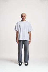 Hvit oversized t-skjorte laget av bomull, paret med løse mørkegrå jeans. Modellen har på seg svarte og hvite sneakers. Enkel, minimalistisk design.