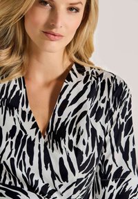 Schwarz-weißes Tiermuster-Wickeloberteil mit tiefem V-Ausschnitt, glattem Stoff und kurzen Ärmeln, das ein strukturiertes Muster aufweist.