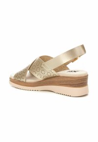 Sandalia de cuña beige, parte superior de cuero con patrones de corte en forma de flor, correa ajustable en el talón, suela con textura similar a la madera, detalle acolchado.