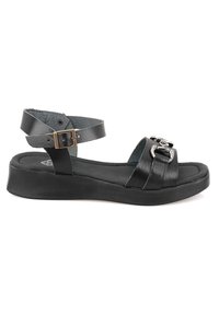 Schwarze Leder-Sandalen mit flacher Sohle, verstellbarem Knöchelriemen und einer metallischen Schnalle auf dem vorderen Riemen. Texturierte Innenauskleidung.
