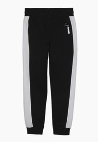 Svarta sweats med grå sidostråk, elastisk midja och en ficka med dragkedja på högra sidan. Mjuk, texturerad stil.