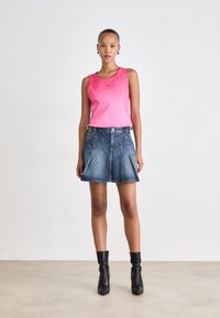 Un top roz fără mâneci, cu o textură subtilă, combinat cu o fustă din denim evazată. Accesoriile includ botine negre până la gleznă.