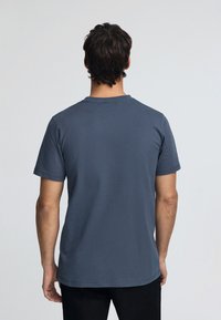 Mörkblå t-shirt med kort ärm i mjuk bomull, med en klassisk rund hals och en avslappnad passform, med minimala sömnadsdetaljer på baksidan.