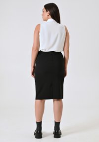 Witte mouwloze blouse met een kraag, gecombineerd met een aansluitende zwarte kokerrok. Zwarte schoenen en donkere sokken. Eenvoudig, eigentijds ontwerp.