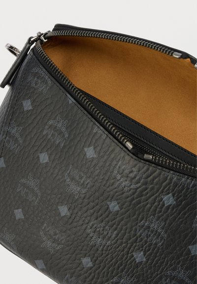 Zwart leren etui met reliëf en MCM-logo patroon. Voorzien van een zilveren rits en een beige voering aan de binnenkant.