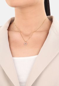Collar de cadena de oro con un colgante circular adornado con piedras transparentes. El colgante presenta una textura suave; la cadena tiene un diseño retorcido.