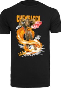 Juodas medvilnės marškinėliai su grafiniu Chewbaccos atvaizdu oranžine ir balta spalva, su stilizuota sprogimo iliustracija ir detaliu laivu fone.