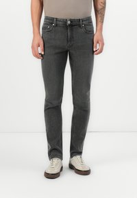 Szürke farmernadrág, slim fit fazonban, cipzáras nyitással, öt zsebbel, és diszkrét koptatással elöl. Világos sportcipővel viselve.