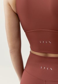 Bordový športový crop top a vysoko pásové legíny z hladkého, elastického materiálu s bielym logom na chrbte.