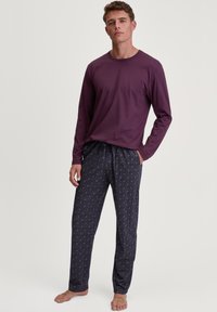 Lange mouwen paarse top gecombineerd met gestreepte pyjamabroek in marineblauw met geometrische ontwerpen in lichte kleuren, gemaakt van zachte stof.