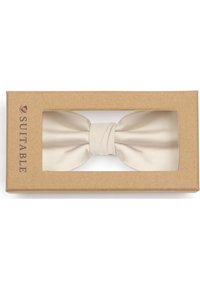 Beige satijnen vlinderdas tentoongesteld in een rechthoekige kartonnen doos met een transparante voorkant. Doos gelabeld "SUITABLE" in donkerblauwe tekst.