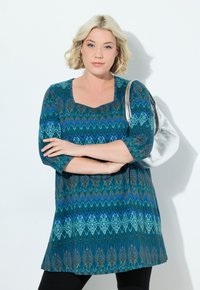 Türkise Tunika mit quadratischem Ausschnitt, ausgestattet mit einem Zickzackmuster in Dunkelblau, Aqua und Braun. Dreiviertelärmel und weicher Stoff.