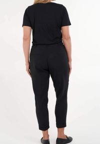 Camiseta negra de cuello redondo combinada con pantalones ajustados negros, con cinturilla elástica y dos bolsillos traseros. Zapatos planos negros completan el look.