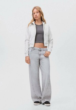Sudadera gris corta con bolsillos frontales, combinada con unos jeans ligeros de corte holgado en color gris claro. Las zapatillas son negras con una suela blanca gruesa.