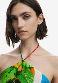 Top a triangolo colorato con una stampa di foglie tropicali nei toni del verde, giallo e blu, con spalline rosse e verdi. Tessuto di alta qualità e morbido.