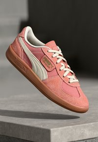 Sneakers Puma s růžovým sametovým a textilním svrškem, akcenty z slonovinové kůže, bílými tkaničkami a texturovanou gumovou podrážkou. Klasické designové prvky.