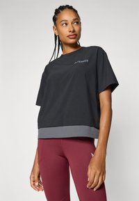 Top negro de manga corta con un dobladillo gris, que presenta un logotipo sutil en el pecho. La tela parece suave y ligera.