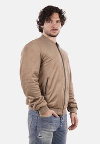Giubbotto bomber in suede beige con zip frontale, polsini a coste e tasca laterale. Il design è minimalista con una texture liscia.