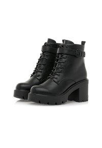 Une paire de bottines en cuir noir avec de gros talons, un devant lacé et des sangles à boucle autour du dessus.