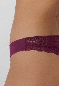 Sous-vêtements hipster en dentelle bordeaux et tissu avec une bordure en dentelle festonnée, texture lisse et ceinture élastique. Vue latérale capturant les détails.