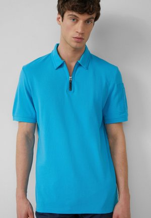 Türkises Poloshirt mit kurzem Reißverschlusskragen, kurzen Ärmeln und einer aufgesetzten Tasche am linken Arm. Glatte Textur, lässige Passform.
