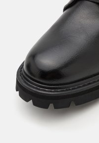 Gros plan sur une botte en cuir noir à bout arrondi et semelle en caoutchouc épaisse et robuste sur fond blanc.