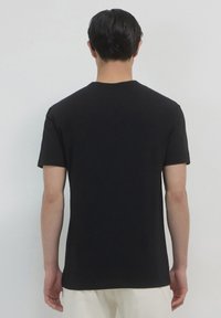 T-shirt in cotone nero con maniche corte, caratterizzato da un colletto tondo e un taglio classico, mostrato dalla vista posteriore su uno sfondo chiaro.