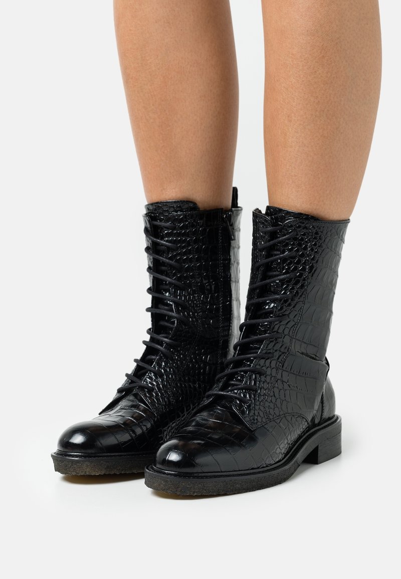 Botines negros de cuero con relieve de cocodrilo, con puntera redondeada, cierre de cordones en la parte delantera, acabado texturizado y tacón bajo de bloque.