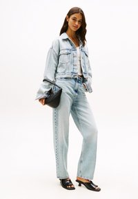 Lyseblå denimjakke med cropped design, kombinert med høyhalsede jeans. Har en svart håndveske og svarte åpen-tå mules.