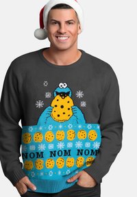 Maglione grigio lavorato a maglia con un design del cookie monster blu, caratterizzato da biscotti gialli, fiocchi di neve e la scritta "NOM NOM NOM" in nero.
