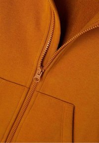 Veste zippée orange avec une texture lisse, dotée d'une fermeture éclair métallique et de détails de couture le long des bords.