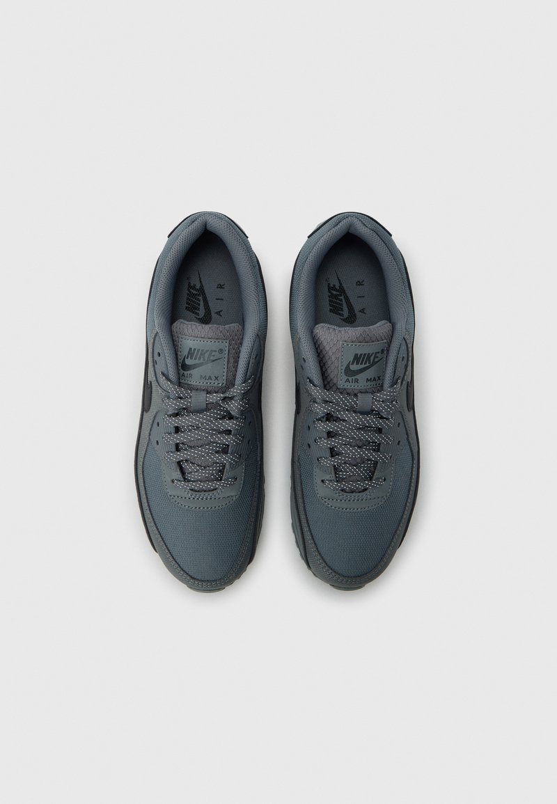 Nike Air Max sneakers in grey, featuring a textured mesh upper, padded collar, and contrasting rubber sole with laces and logo detail.