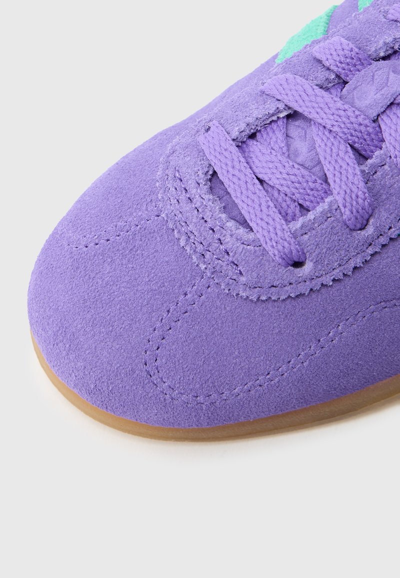 Lila Wildledersneaker mit rundlicher Zehenkappe, strukturierter Oberfläche und passenden Schnürsenkeln. Verfügt über grüne Akzente und eine braune Gummisohle.