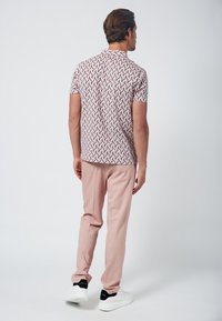Camisa de manga corta con un patrón geométrico rojo y blanco, combinada con pantalones suaves rosa y zapatillas blancas con detalles en negro.